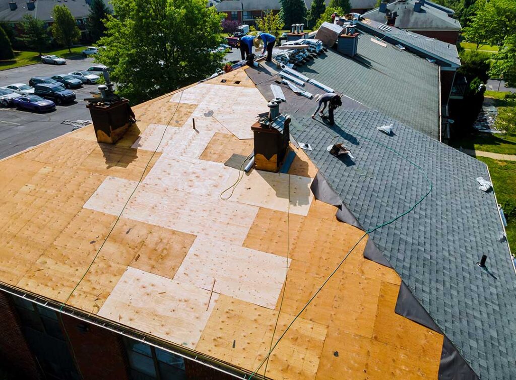 A roofer inspecting flashing around a plumbing vent on a shingled roof with tools nearby